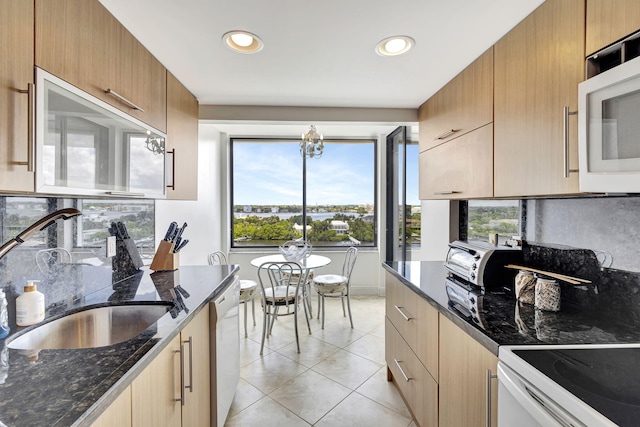 kitchen with sink, white appliances, light tile patterned floors, dark stone countertops, and an inviting chandelier