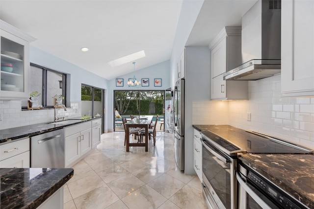 kitchen featuring decorative light fixtures, stainless steel appliances, white cabinets, tasteful backsplash, and wall chimney exhaust hood