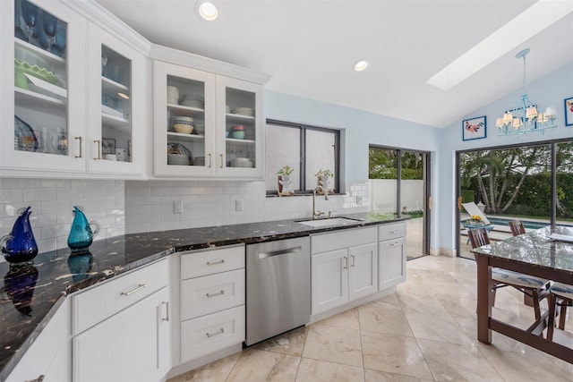 kitchen with stainless steel dishwasher, vaulted ceiling with skylight, a notable chandelier, dark stone countertops, and sink