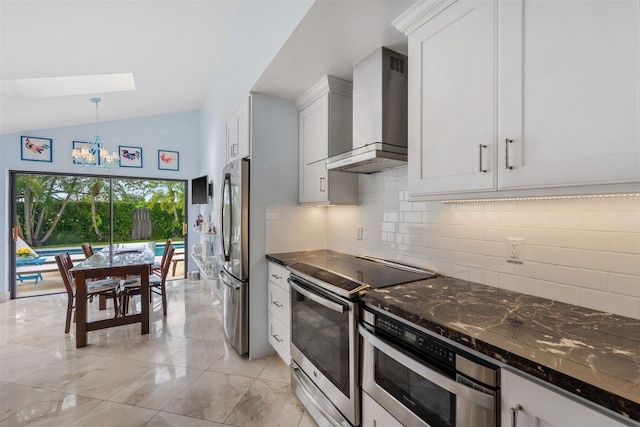 kitchen featuring white cabinetry, decorative light fixtures, stainless steel appliances, lofted ceiling with skylight, and wall chimney exhaust hood