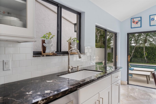 kitchen with dark stone counters, light tile flooring, vaulted ceiling, white cabinets, and sink