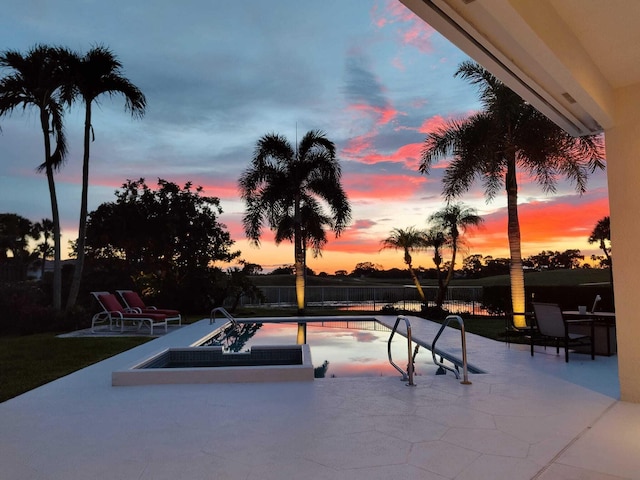 pool at dusk with a patio and a hot tub