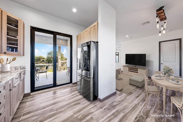 kitchen with wood finish floors, visible vents, stainless steel refrigerator with ice dispenser, glass insert cabinets, and light stone countertops