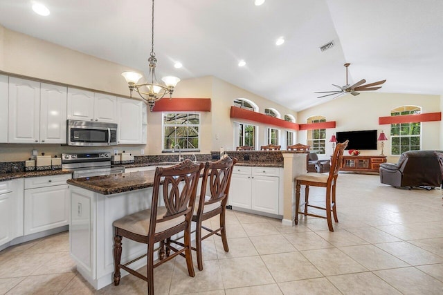 kitchen featuring ceiling fan with notable chandelier, a breakfast bar, stainless steel appliances, hanging light fixtures, and lofted ceiling