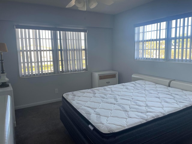 bedroom with ceiling fan, dark colored carpet, and multiple windows