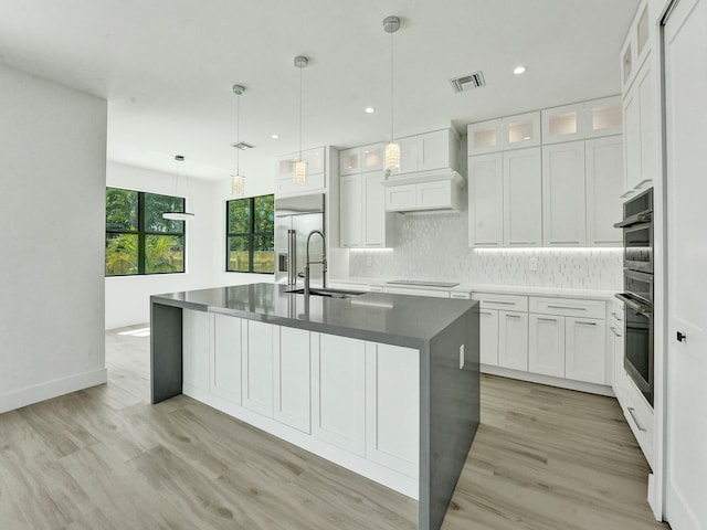 kitchen with white cabinets, decorative light fixtures, custom range hood, and light wood-type flooring