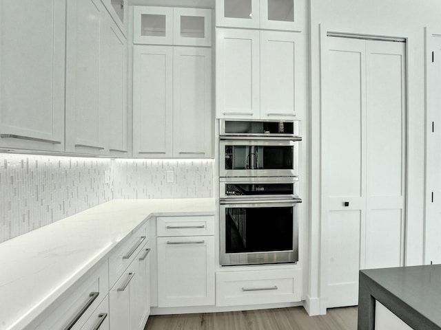 kitchen featuring white cabinets, backsplash, double oven, and light wood-type flooring