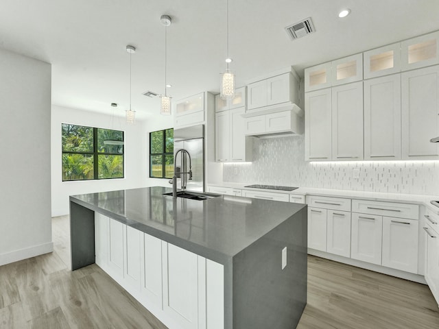 kitchen with light hardwood / wood-style flooring, hanging light fixtures, white cabinetry, and an island with sink