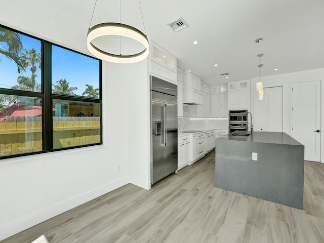 kitchen featuring pendant lighting, light hardwood / wood-style floors, tasteful backsplash, appliances with stainless steel finishes, and white cabinets