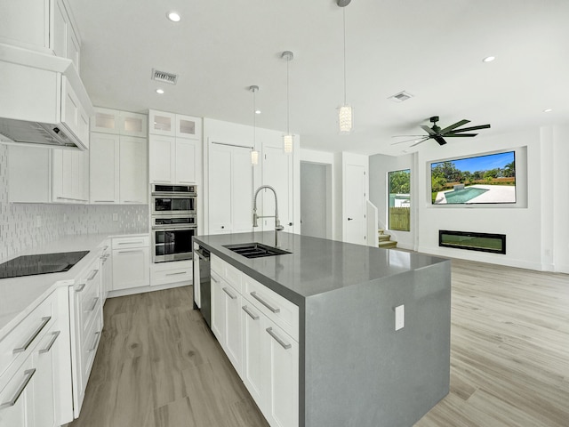 kitchen featuring a kitchen island with sink, white cabinets, stainless steel appliances, and light wood-type flooring