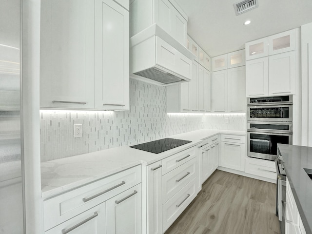 kitchen featuring custom range hood, black electric stovetop, stainless steel double oven, white cabinetry, and light hardwood / wood-style flooring