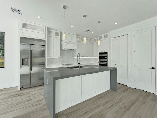 kitchen with appliances with stainless steel finishes, backsplash, light hardwood / wood-style flooring, and white cabinetry