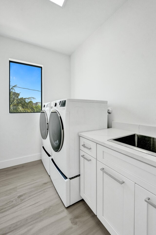 washroom featuring washing machine and dryer, cabinets, and light wood-type flooring