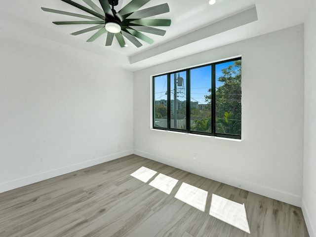 empty room featuring ceiling fan, light wood-type flooring, and a raised ceiling