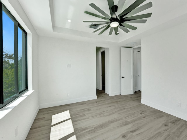 spare room with a raised ceiling, ceiling fan, and light hardwood / wood-style flooring