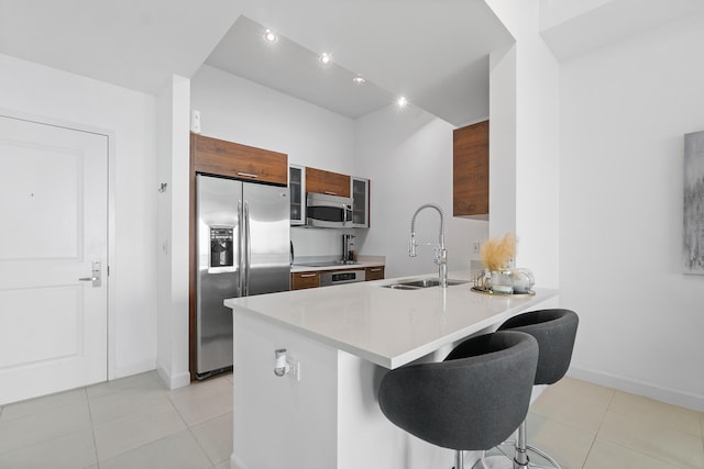 kitchen with light tile patterned flooring, sink, a kitchen bar, kitchen peninsula, and stainless steel appliances