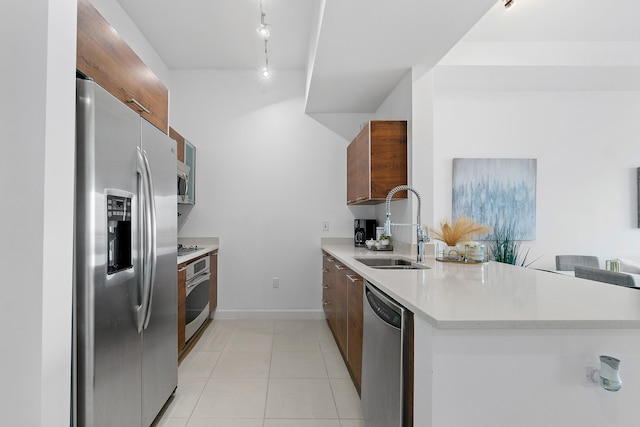 kitchen with rail lighting, sink, light tile patterned floors, appliances with stainless steel finishes, and kitchen peninsula