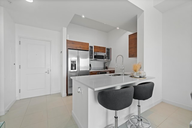 kitchen with sink, light tile patterned floors, a kitchen breakfast bar, kitchen peninsula, and stainless steel appliances