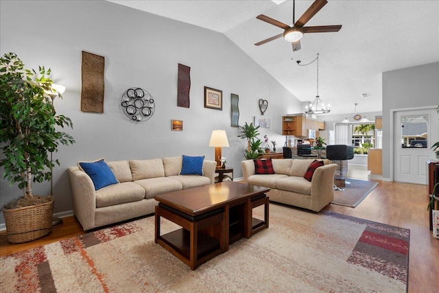 living room with high vaulted ceiling, wood-type flooring, and ceiling fan with notable chandelier