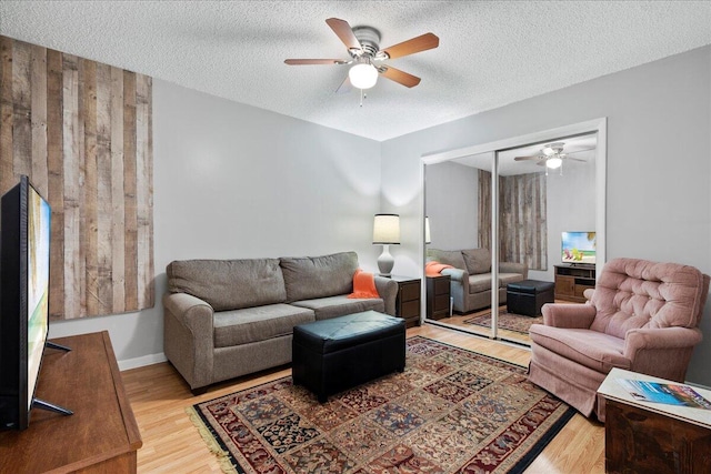 living room with ceiling fan, a textured ceiling, and light hardwood / wood-style flooring