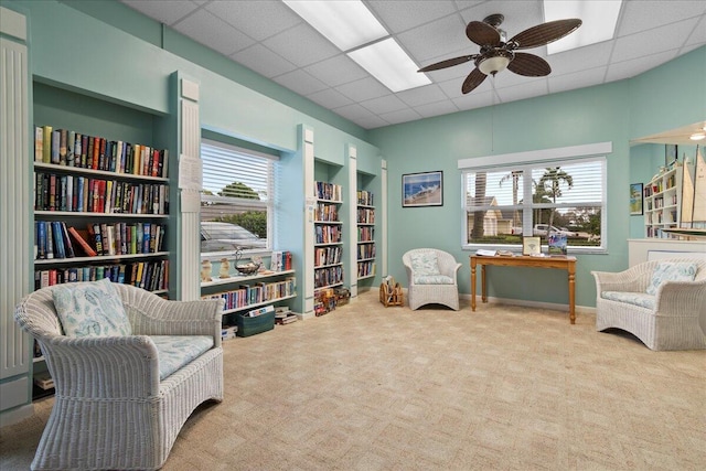 sitting room with a wealth of natural light, ceiling fan, carpet flooring, and a drop ceiling