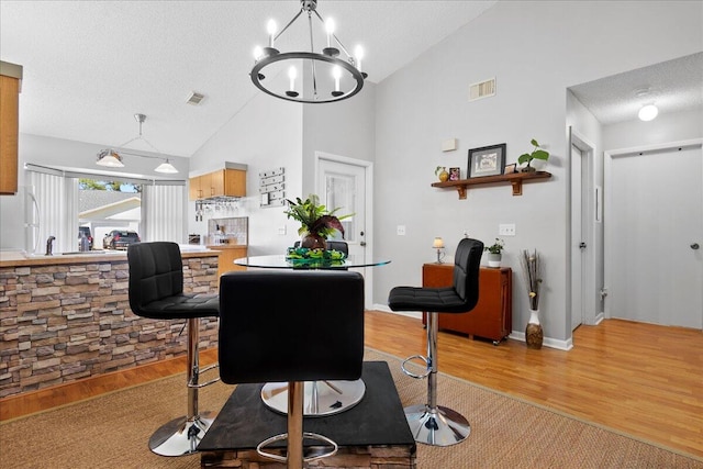 dining room featuring a notable chandelier, a textured ceiling, high vaulted ceiling, and hardwood / wood-style floors