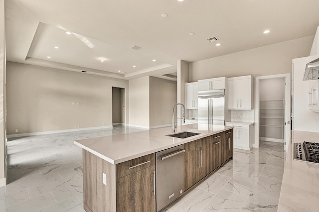 kitchen with sink, an island with sink, appliances with stainless steel finishes, white cabinetry, and dark brown cabinetry