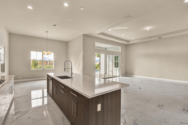 kitchen featuring dark brown cabinets, sink, pendant lighting, a notable chandelier, and an island with sink