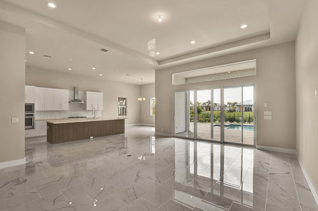 kitchen featuring white cabinets, a raised ceiling, sink, wall chimney exhaust hood, and a large island