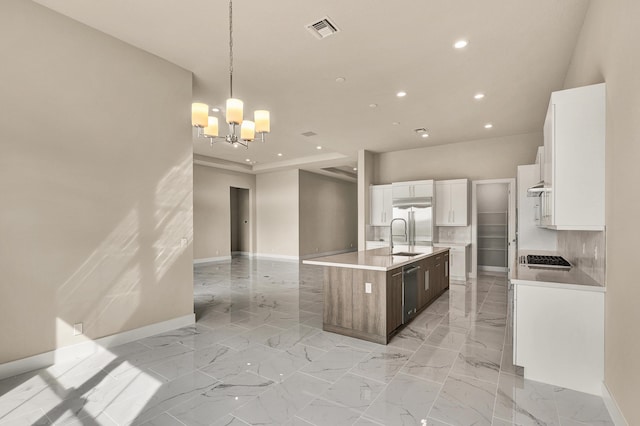 kitchen featuring pendant lighting, backsplash, a center island with sink, white cabinets, and a notable chandelier