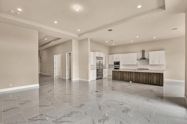 kitchen with white cabinets, a raised ceiling, wall chimney range hood, built in appliances, and a large island