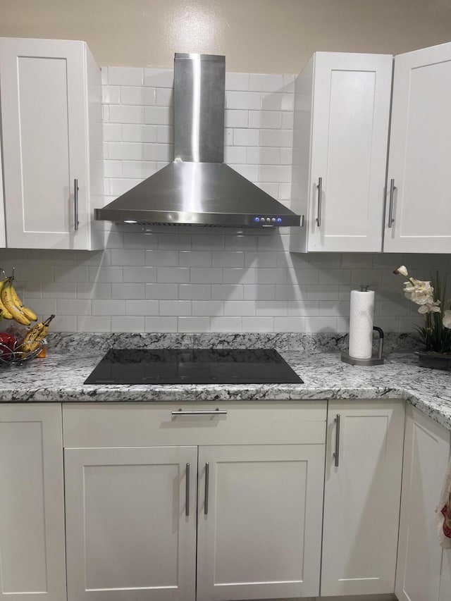 kitchen featuring wall chimney exhaust hood, tasteful backsplash, and white cabinetry