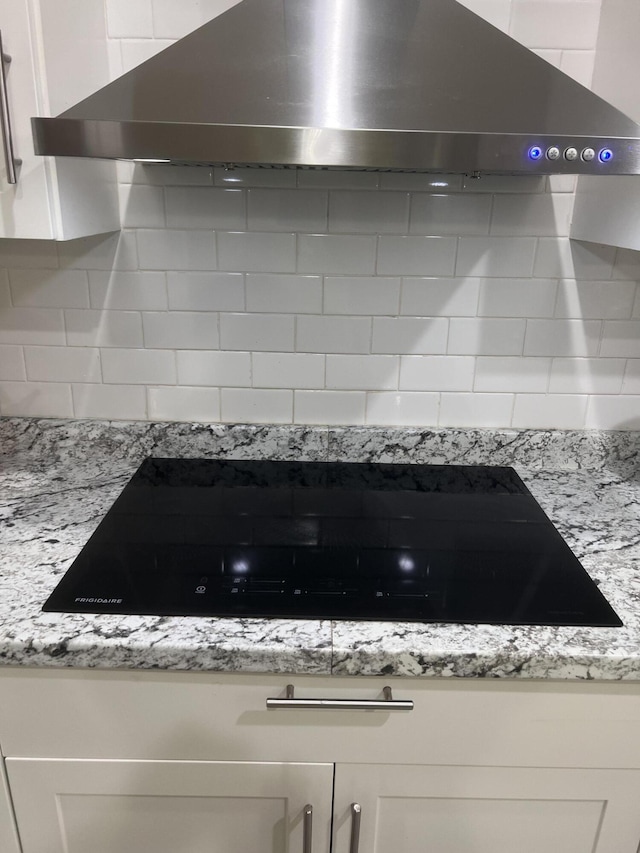 room details featuring black stovetop, backsplash, and wall chimney range hood