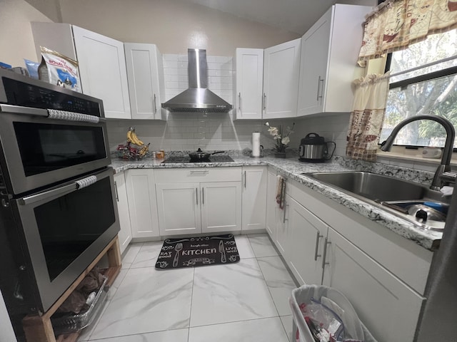 kitchen featuring double wall oven, wall chimney exhaust hood, backsplash, and white cabinetry