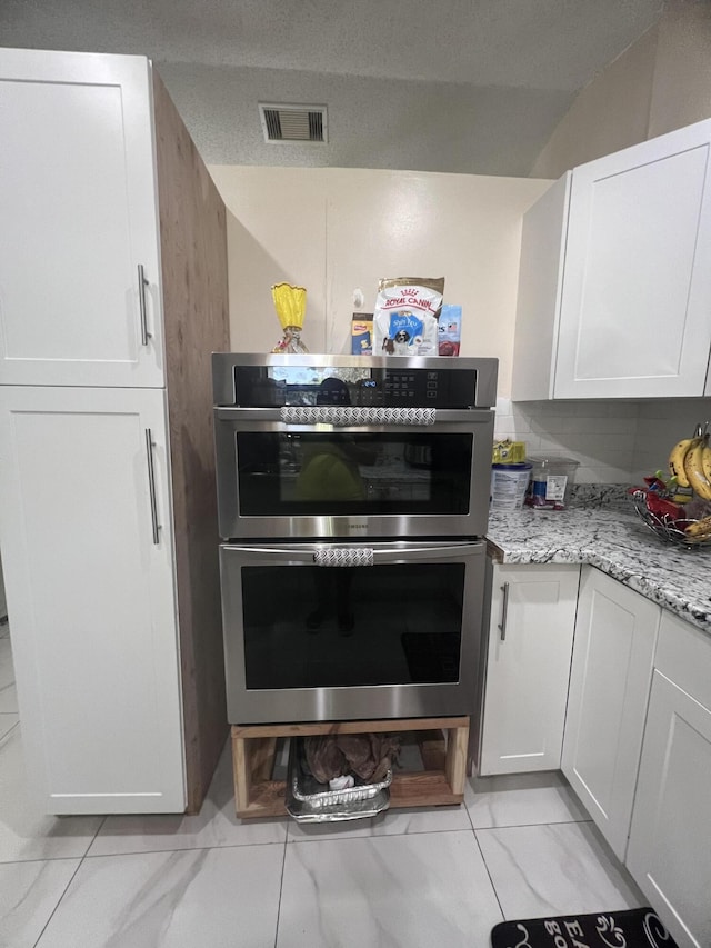 kitchen featuring light stone countertops, white cabinetry, stainless steel double oven, and light tile flooring