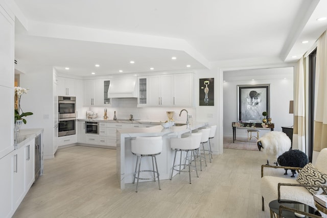 kitchen with stainless steel double oven, custom range hood, light hardwood / wood-style flooring, and white cabinetry