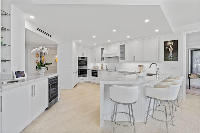 kitchen with kitchen peninsula, white cabinetry, light wood-type flooring, premium range hood, and light stone counters