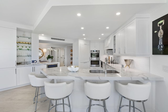 kitchen featuring white cabinets, kitchen peninsula, light stone countertops, and double oven