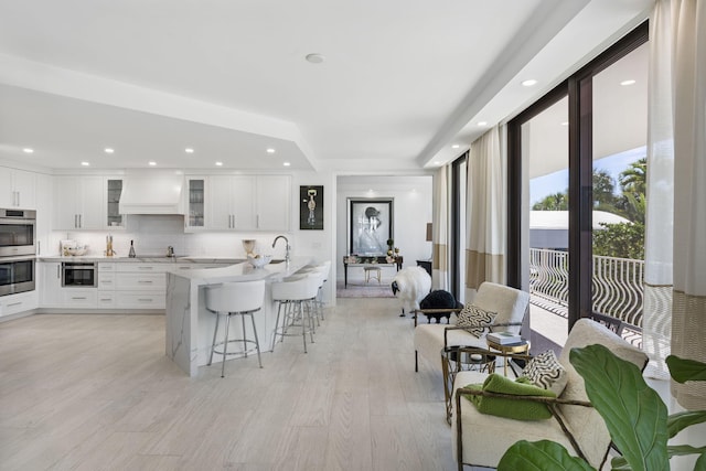 kitchen with stainless steel double oven, a kitchen bar, custom exhaust hood, and white cabinetry