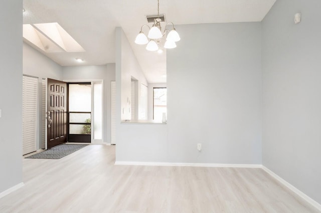 spare room featuring a skylight, a chandelier, and light hardwood / wood-style flooring