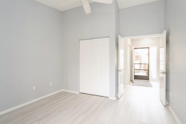 unfurnished bedroom featuring a high ceiling, a closet, ceiling fan, and light wood-type flooring