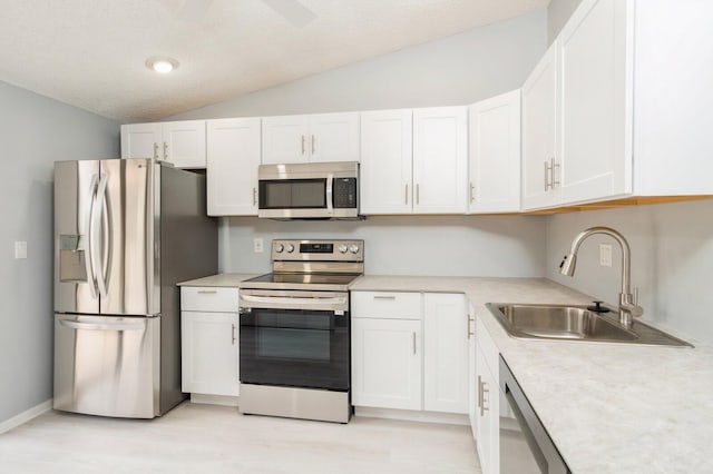 kitchen with sink, white cabinets, appliances with stainless steel finishes, vaulted ceiling, and light wood-type flooring