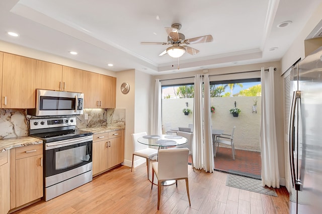 kitchen featuring light hardwood / wood-style flooring, stainless steel appliances, tasteful backsplash, a tray ceiling, and light brown cabinetry