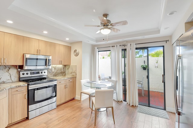 kitchen with appliances with stainless steel finishes, light brown cabinetry, decorative backsplash, a tray ceiling, and light hardwood / wood-style flooring