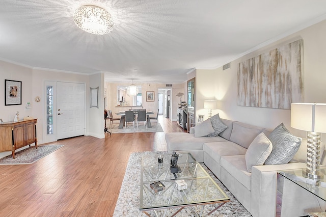 living room with crown molding, a notable chandelier, and light hardwood / wood-style flooring