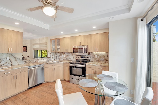 kitchen featuring light stone counters, light brown cabinets, a tray ceiling, stainless steel appliances, and decorative backsplash