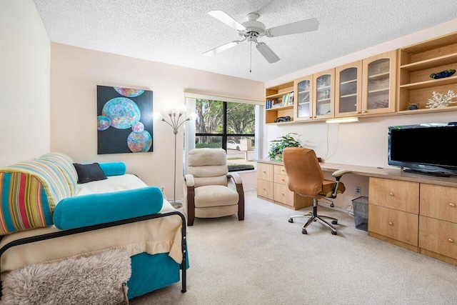 office with ceiling fan, light colored carpet, built in desk, and a textured ceiling