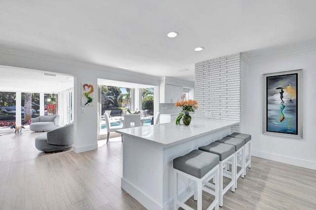 kitchen featuring brick wall, light hardwood / wood-style flooring, a kitchen breakfast bar, white cabinetry, and ornamental molding