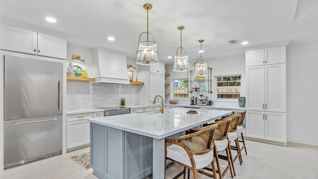 kitchen featuring premium range hood, light tile floors, built in refrigerator, backsplash, and range