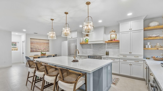 kitchen with an island with sink, light tile floors, premium range hood, tasteful backsplash, and pendant lighting